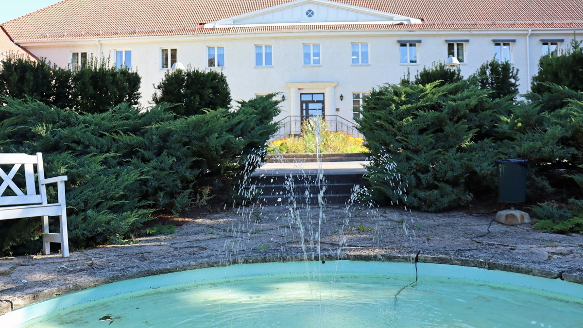 Bild på en fontän samt Vara folkhögskolas huvudbyggnad i bakgrunden