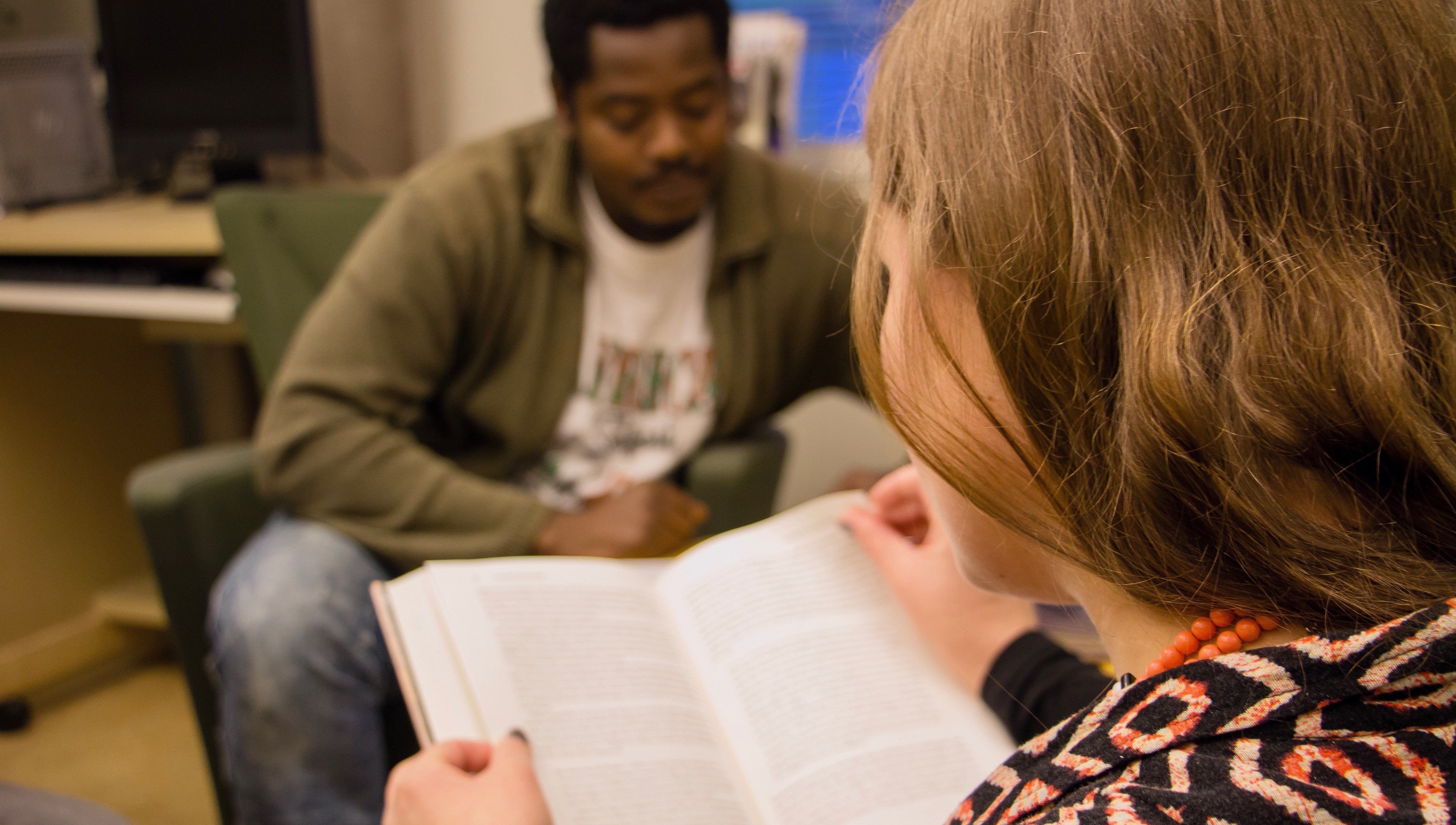 En folkhögskoledeltagare som läser i en bok. I bakgrunden ser vi en annan folkhögskoledeltagare.