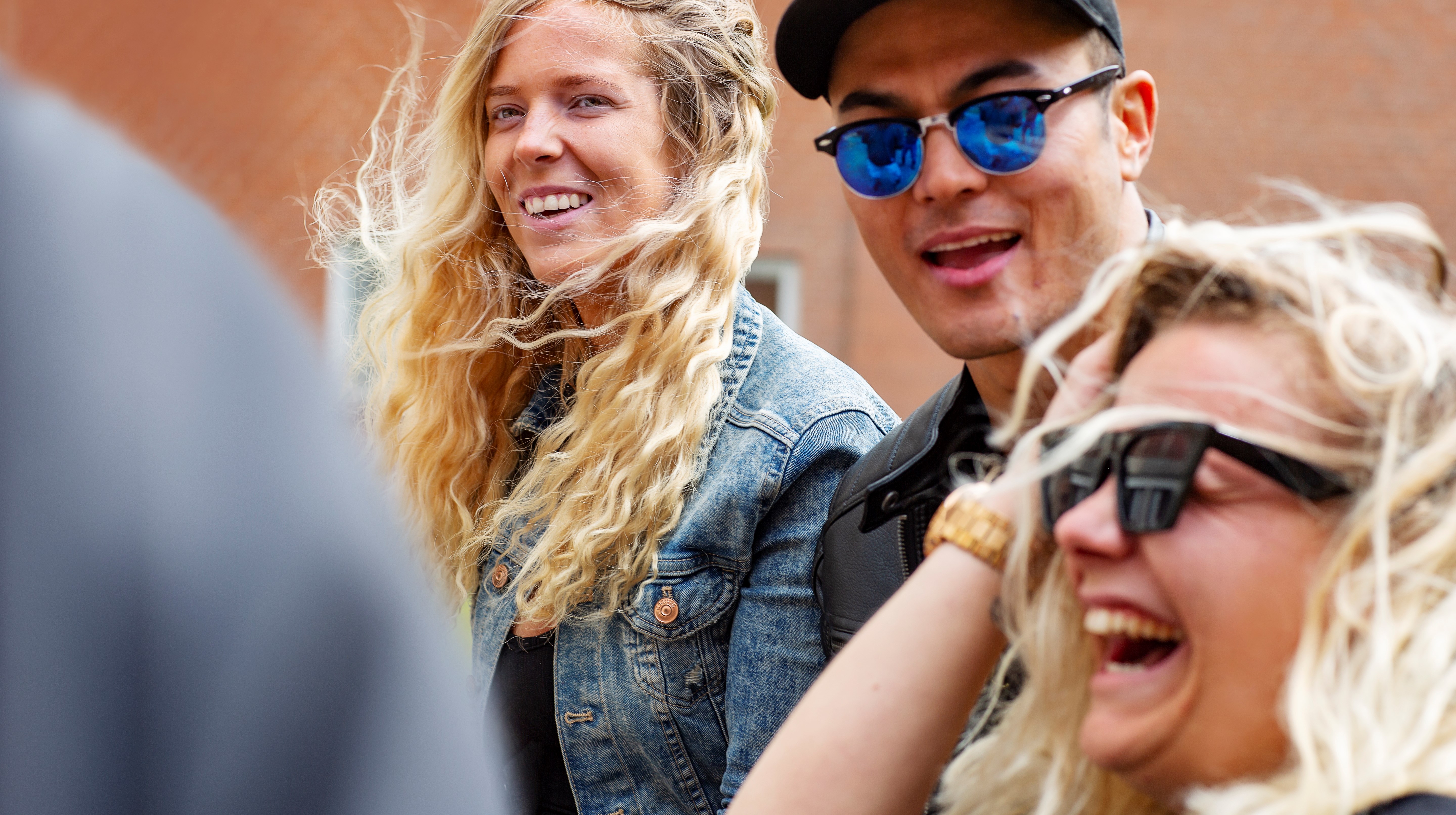 Tre personer utomhus i blåsten. Två personer har solglasögon.