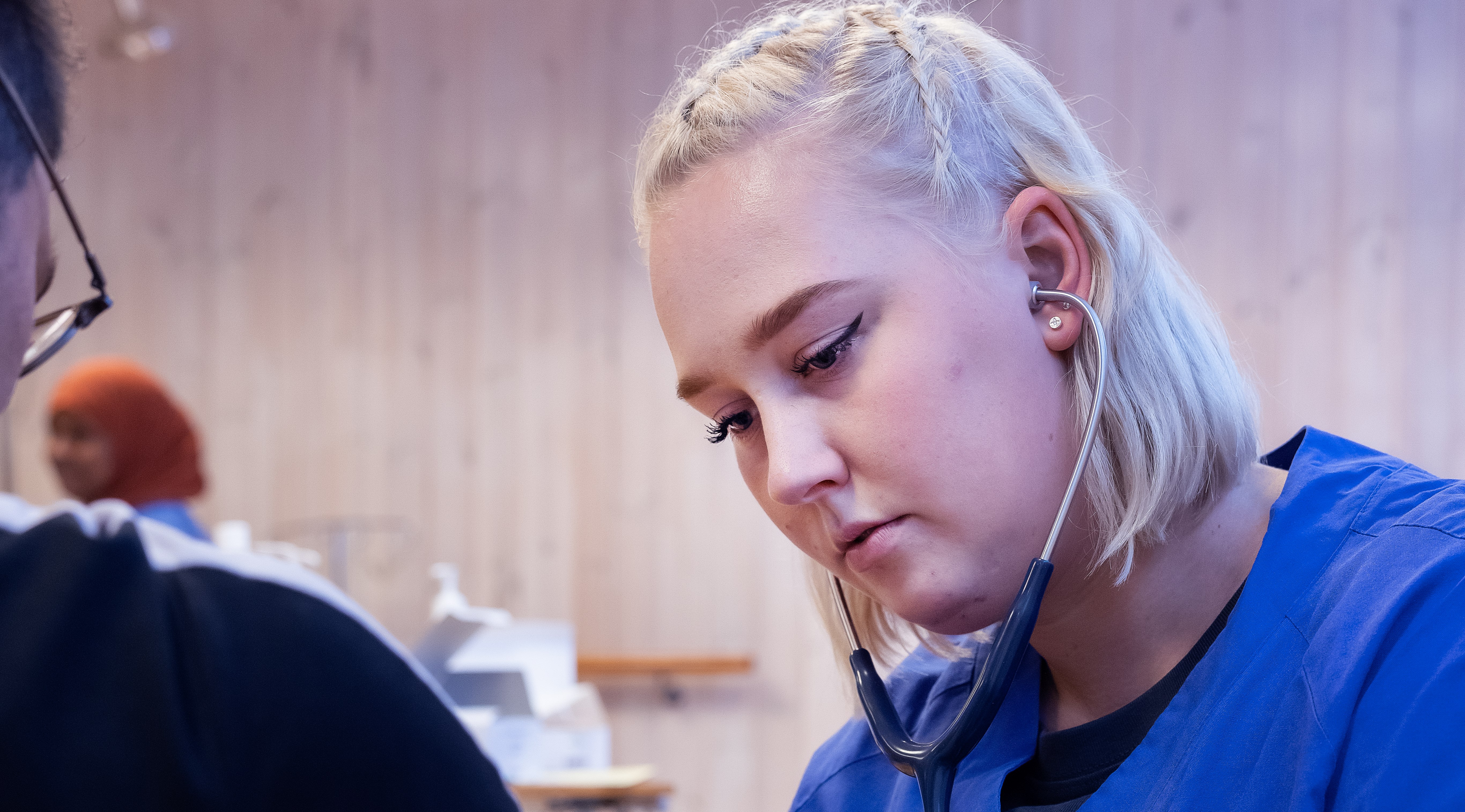 En folkhögskoledeltagare som läser till undersköterska som hjälper en sittande person.